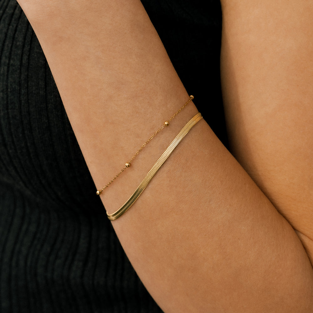Gold anklets on a person's ankle against a black background