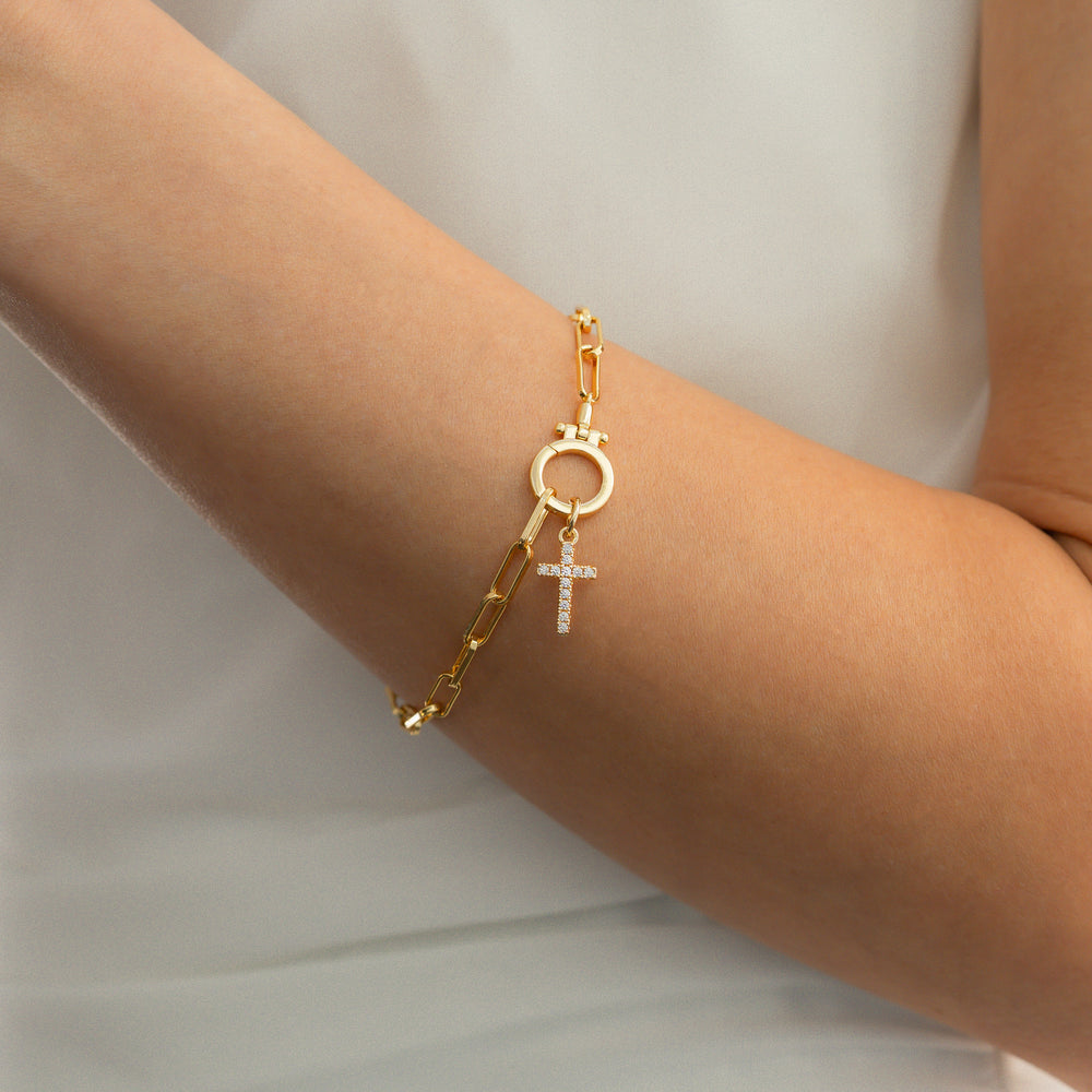 Gold bracelet with a cross charm on a wrist against a neutral background