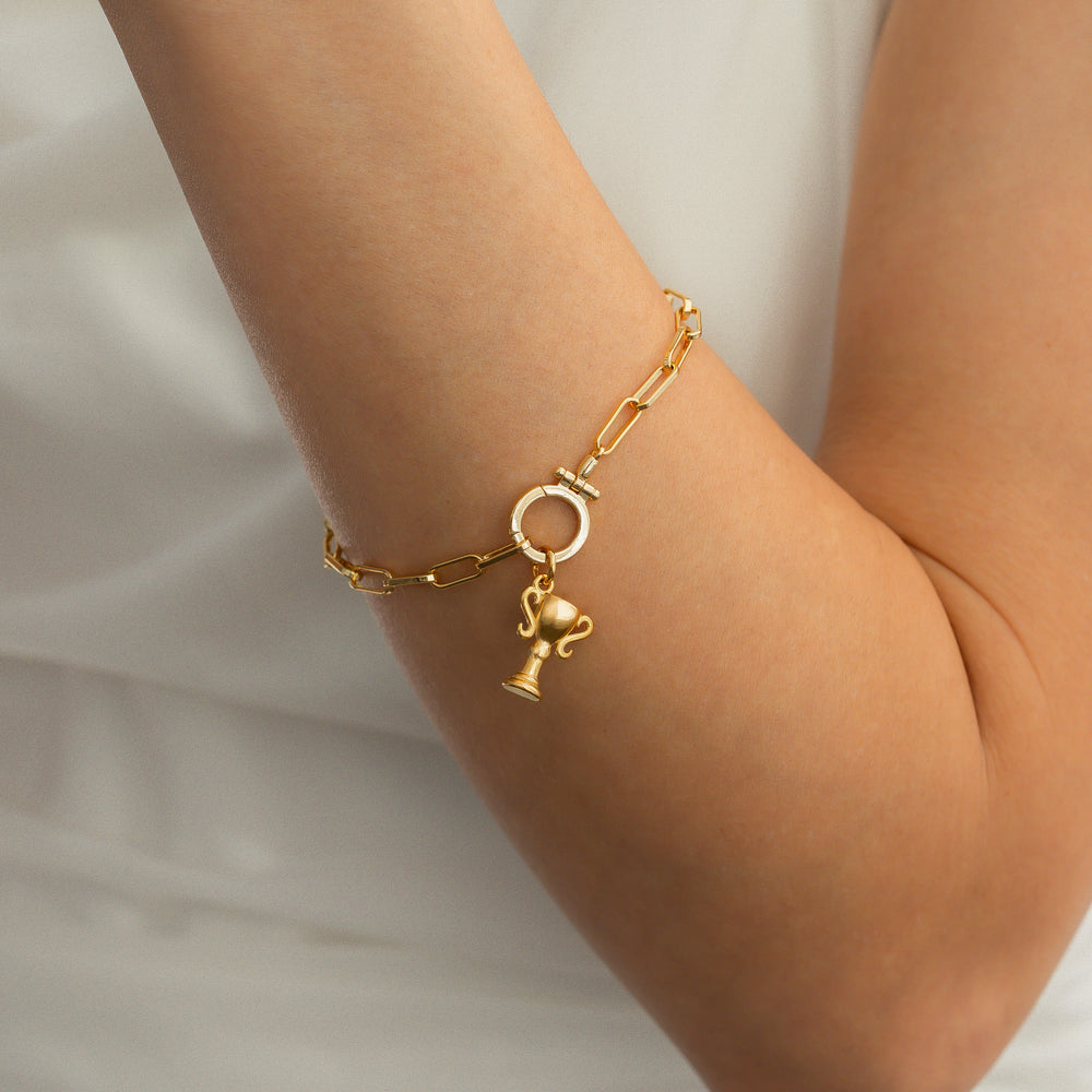 Gold bracelet with a trophy charm on a person's wrist against a neutral background
