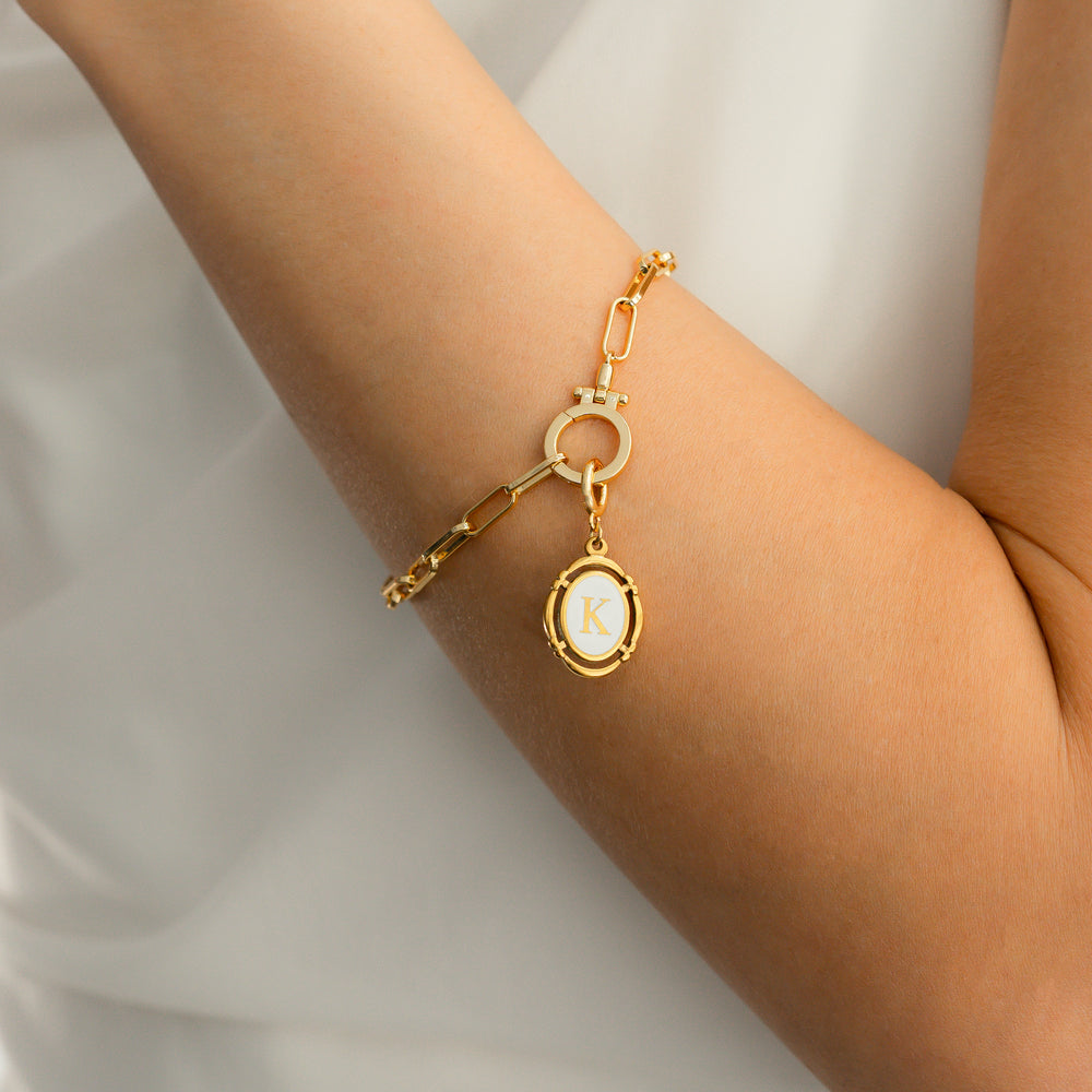 Gold bracelet with a circular charm on a person's wrist against a neutral background