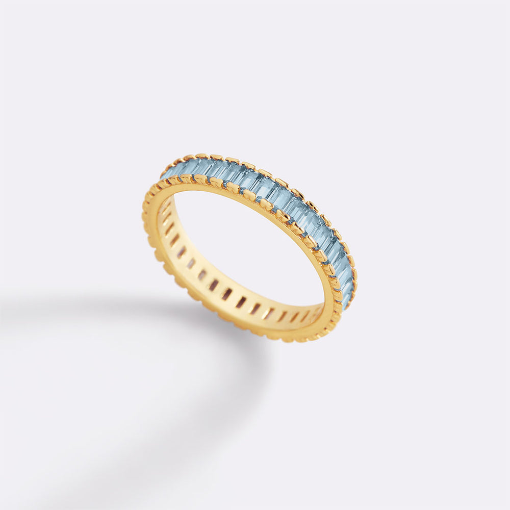 Gold ring with blue gemstones on a light gray background