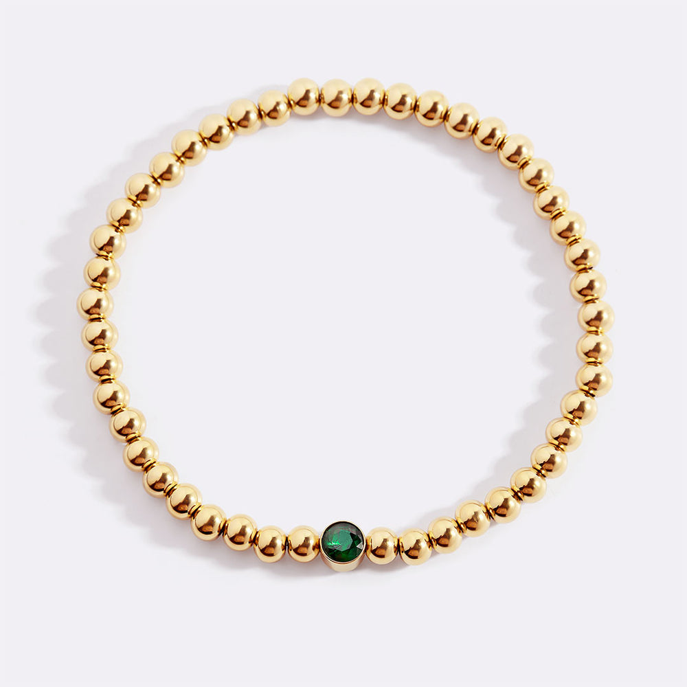 Gold beaded bracelet with a green gemstone on a white background