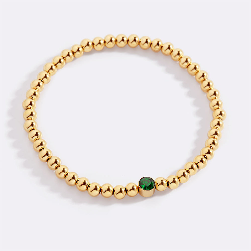 Gold beaded bracelet with a green gemstone on a white background