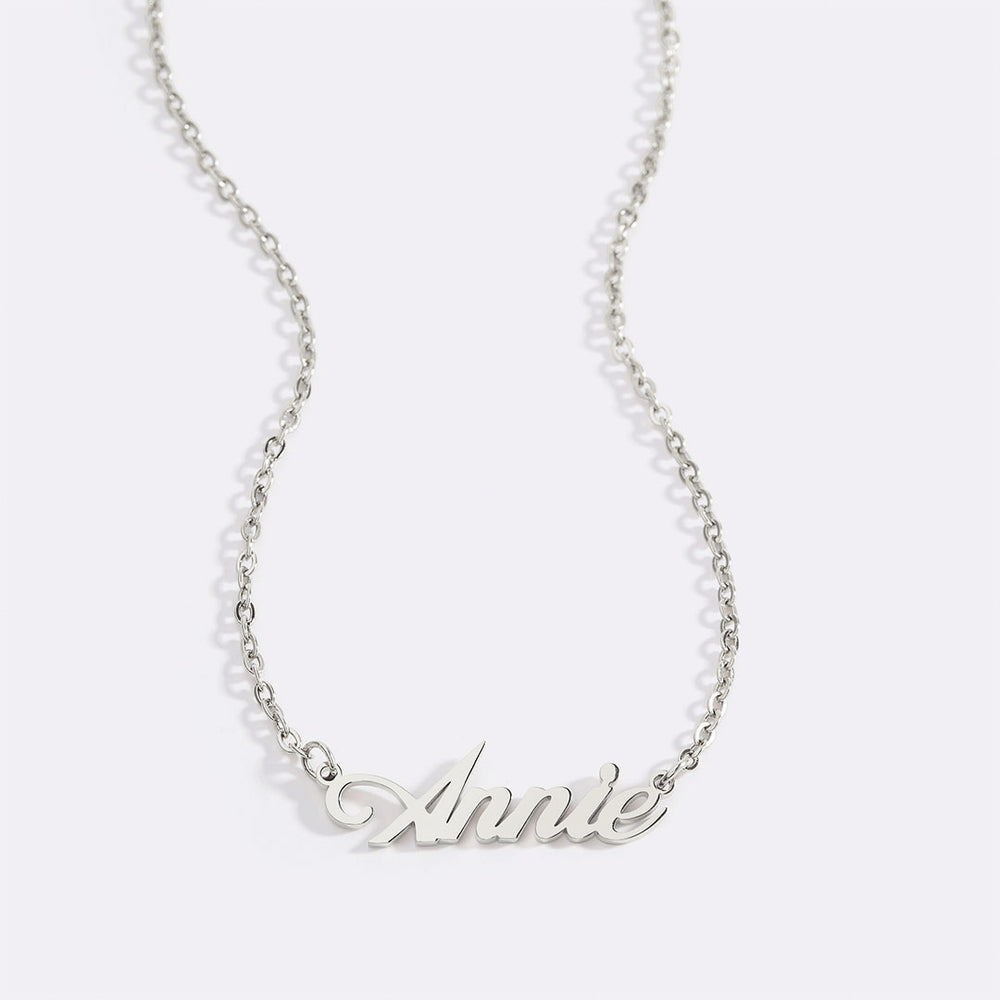 A gold name necklace with the name 'Annie' written in a cursive script on a chain.