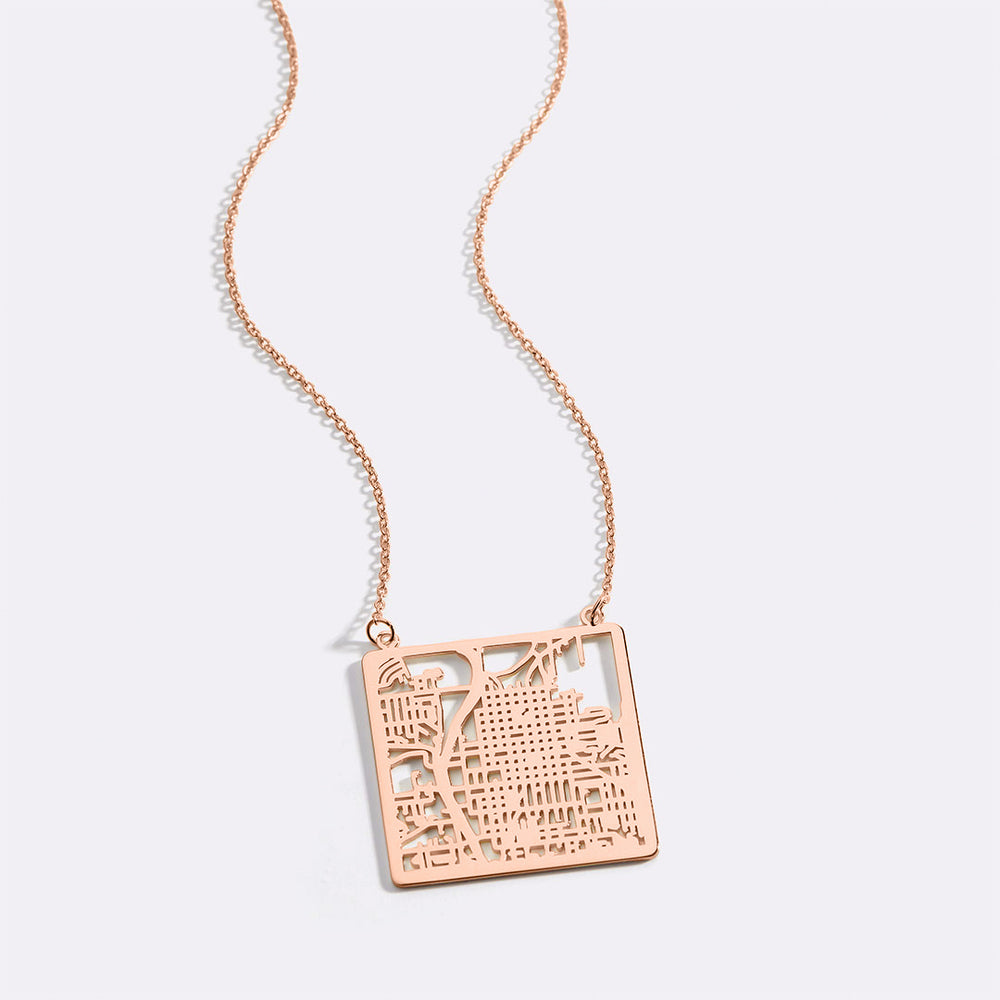 A gold vermeil necklace with a circular pendant featuring a detailed map inscribed on it, displayed against a black background.