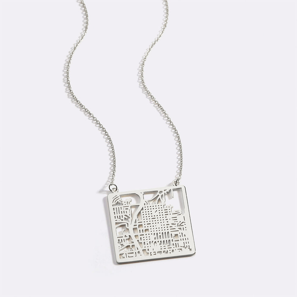 A gold vermeil necklace with a circular pendant featuring a detailed map inscribed on it, displayed against a black background.