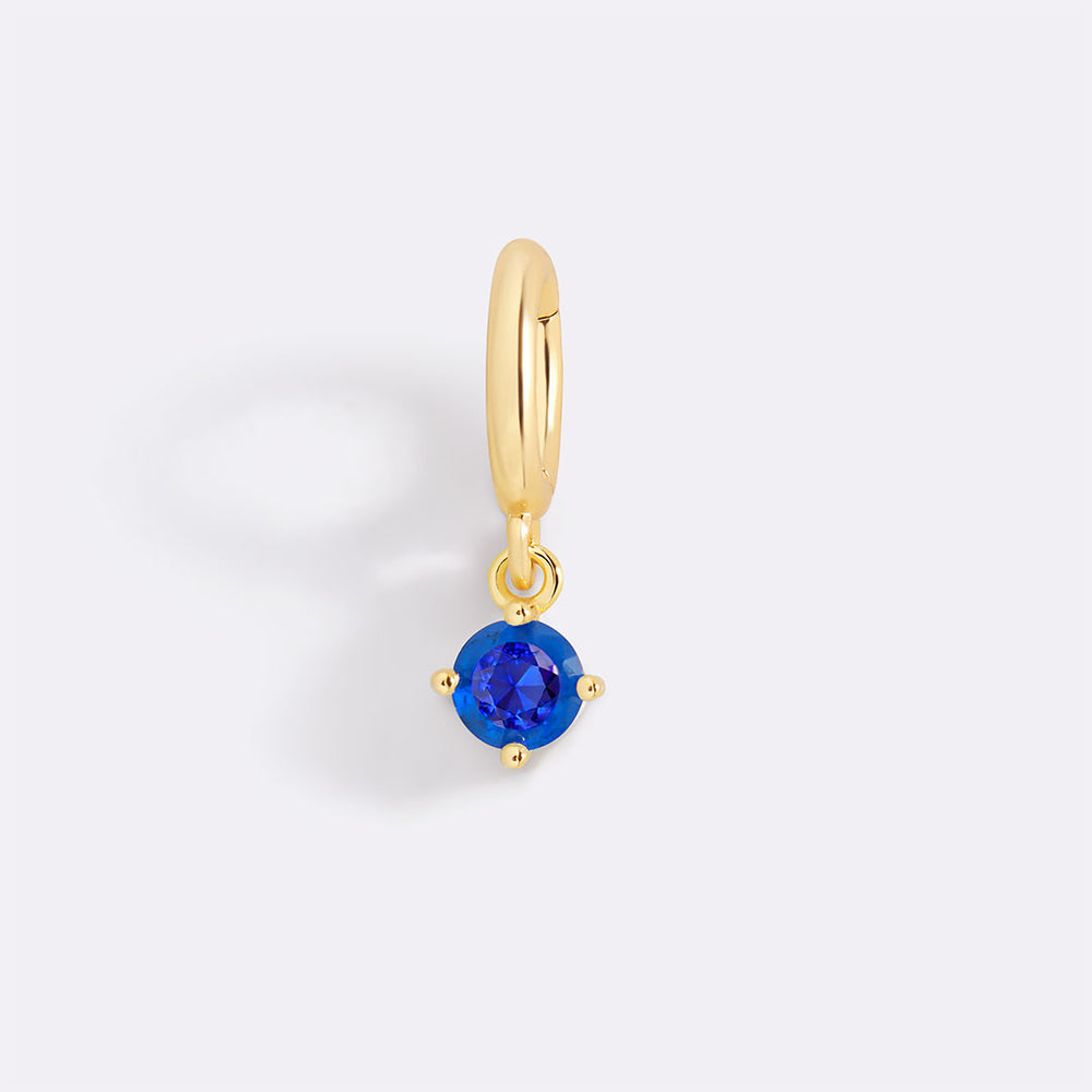 Gold earring with a blue gemstone on a light gray background