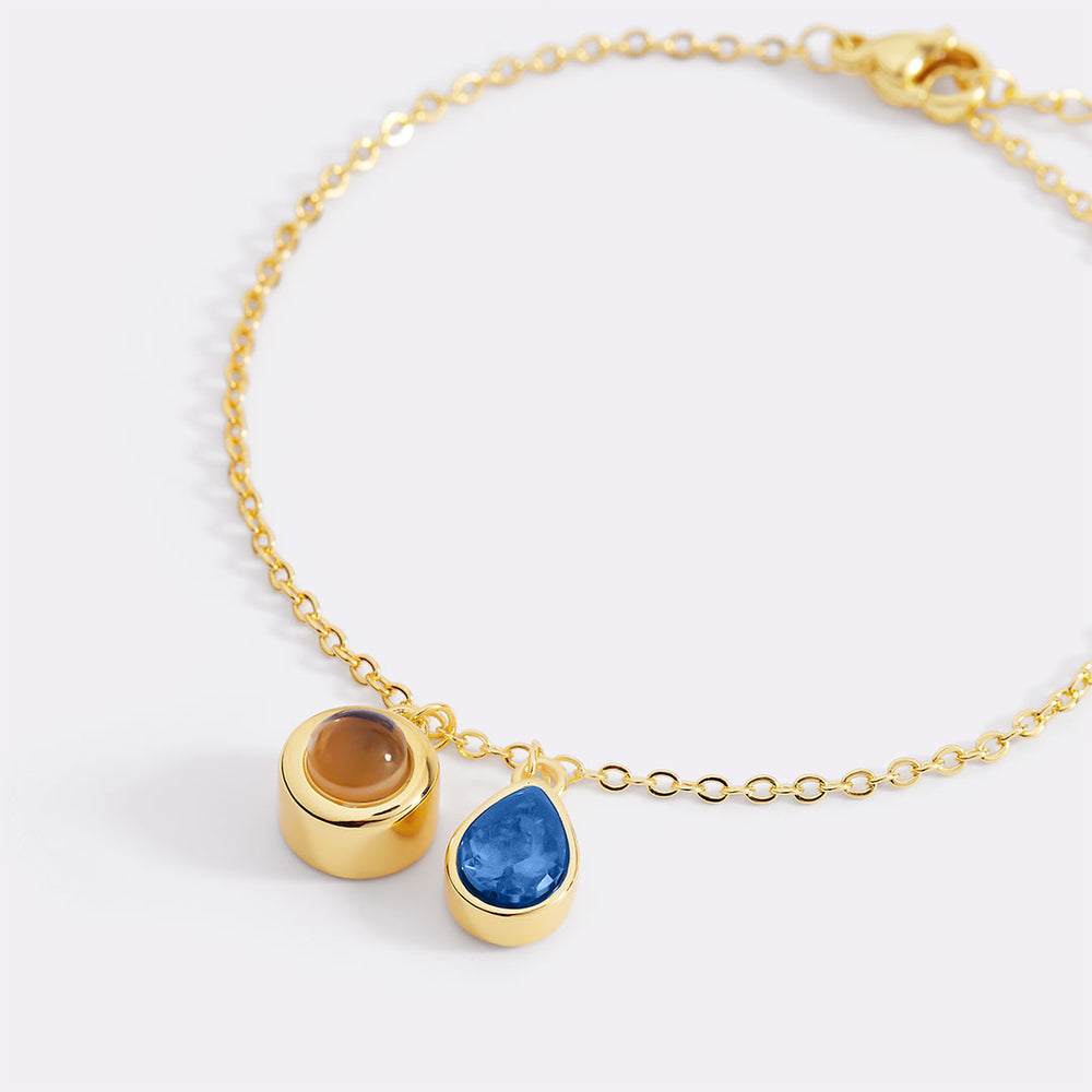 Gold bracelet with two gemstone charms on a white background