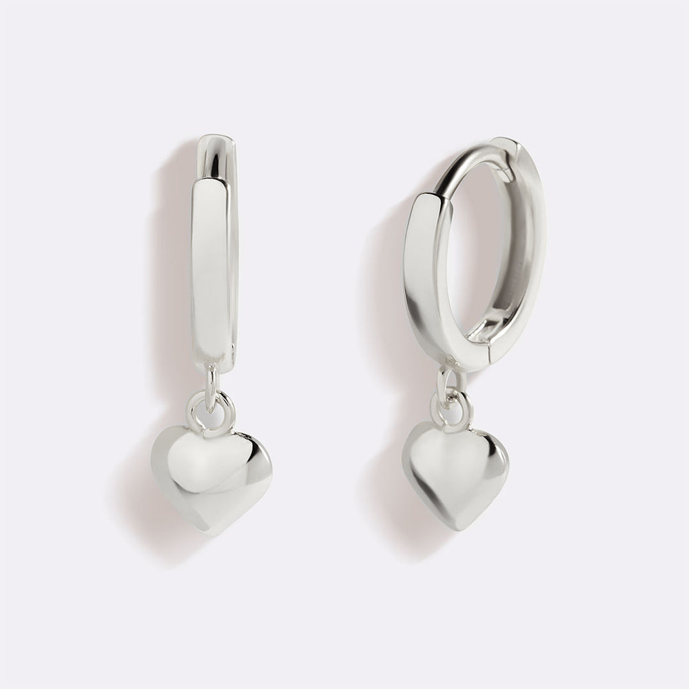 Silver hoop earrings with heart-shaped charms on a light gray background