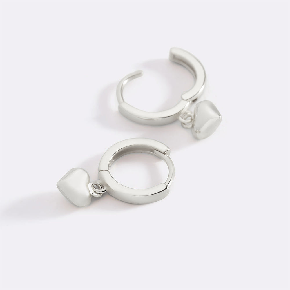 Pair of silver hoop earrings with heart charms on a white background