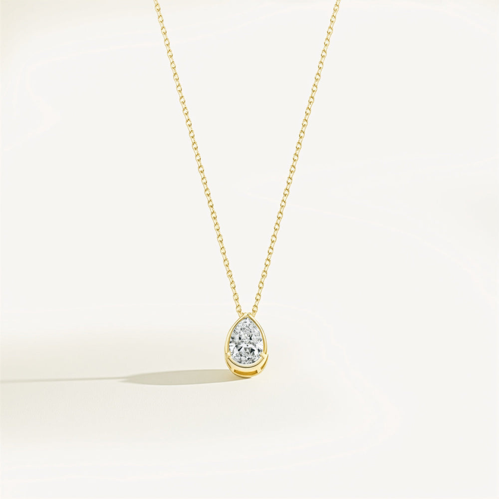 Gold necklace with a teardrop-shaped moissanite pendant on a light beige background