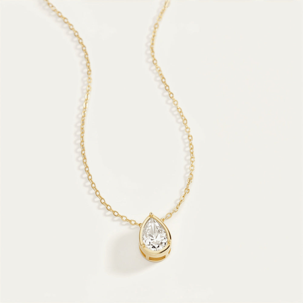 Gold necklace with a teardrop-shaped moissanite pendant on a light gray background