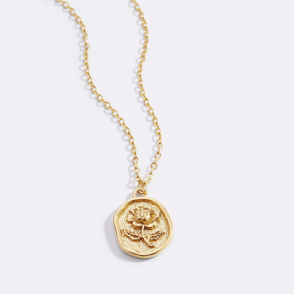 A gold-colored pendant necklace with a detailed rose stamp on the pendant, displayed against a white background.
