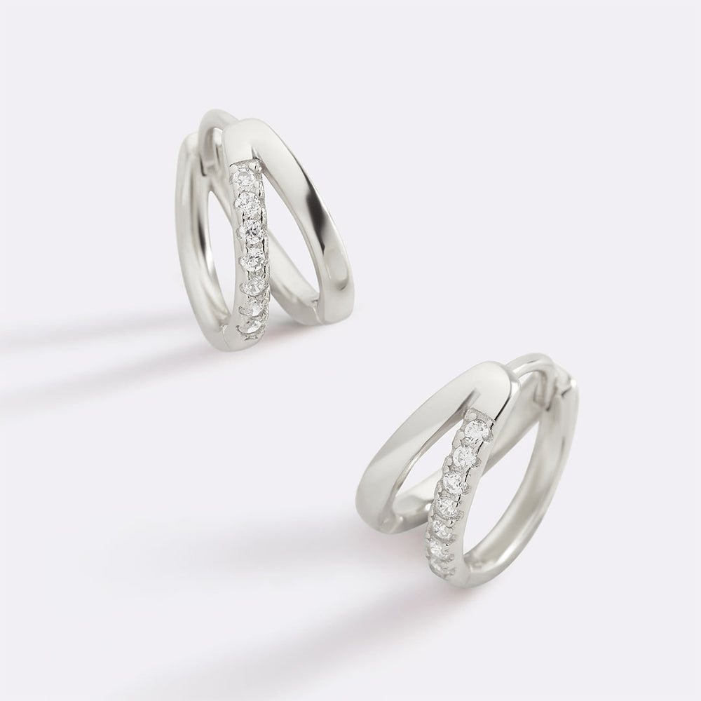 Pair of silver hoop earrings with small diamonds on a light gray background