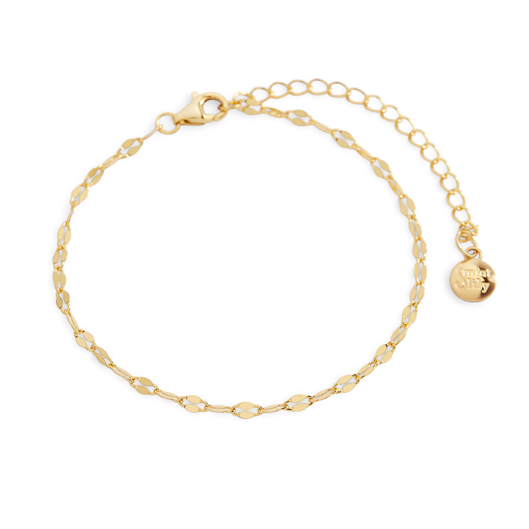Gold bracelet with a small round charm on a light gray background