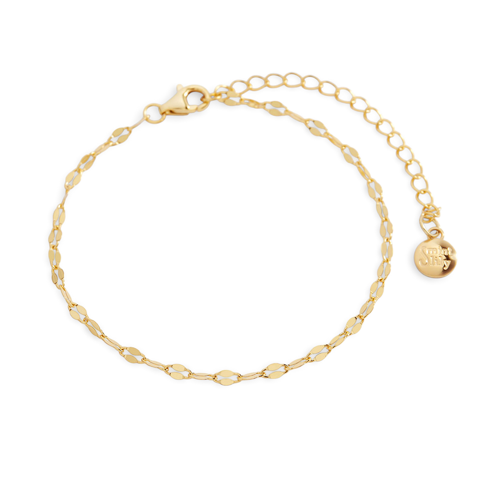 Gold bracelet with a small round charm on a light gray background