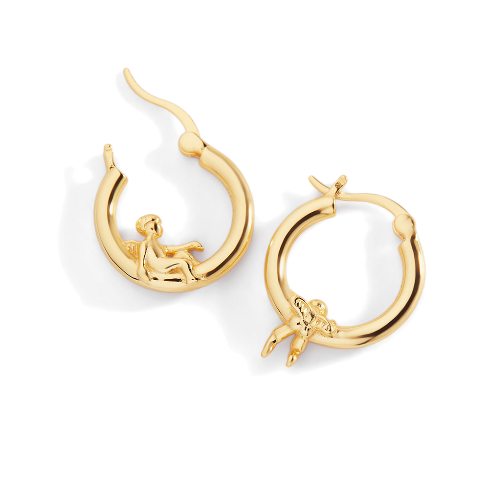 Gold hoop earrings with a small figure design on a white background