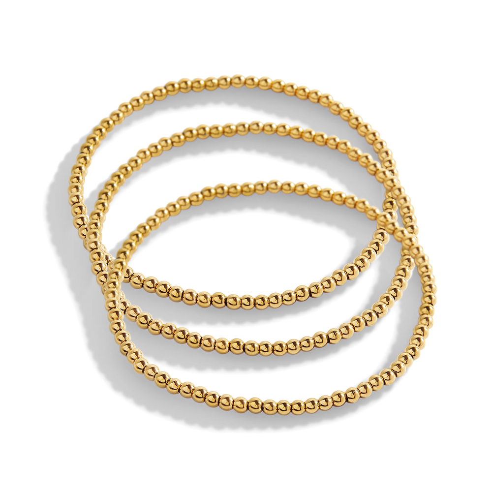 Set of three gold beaded bracelets on a light gray background