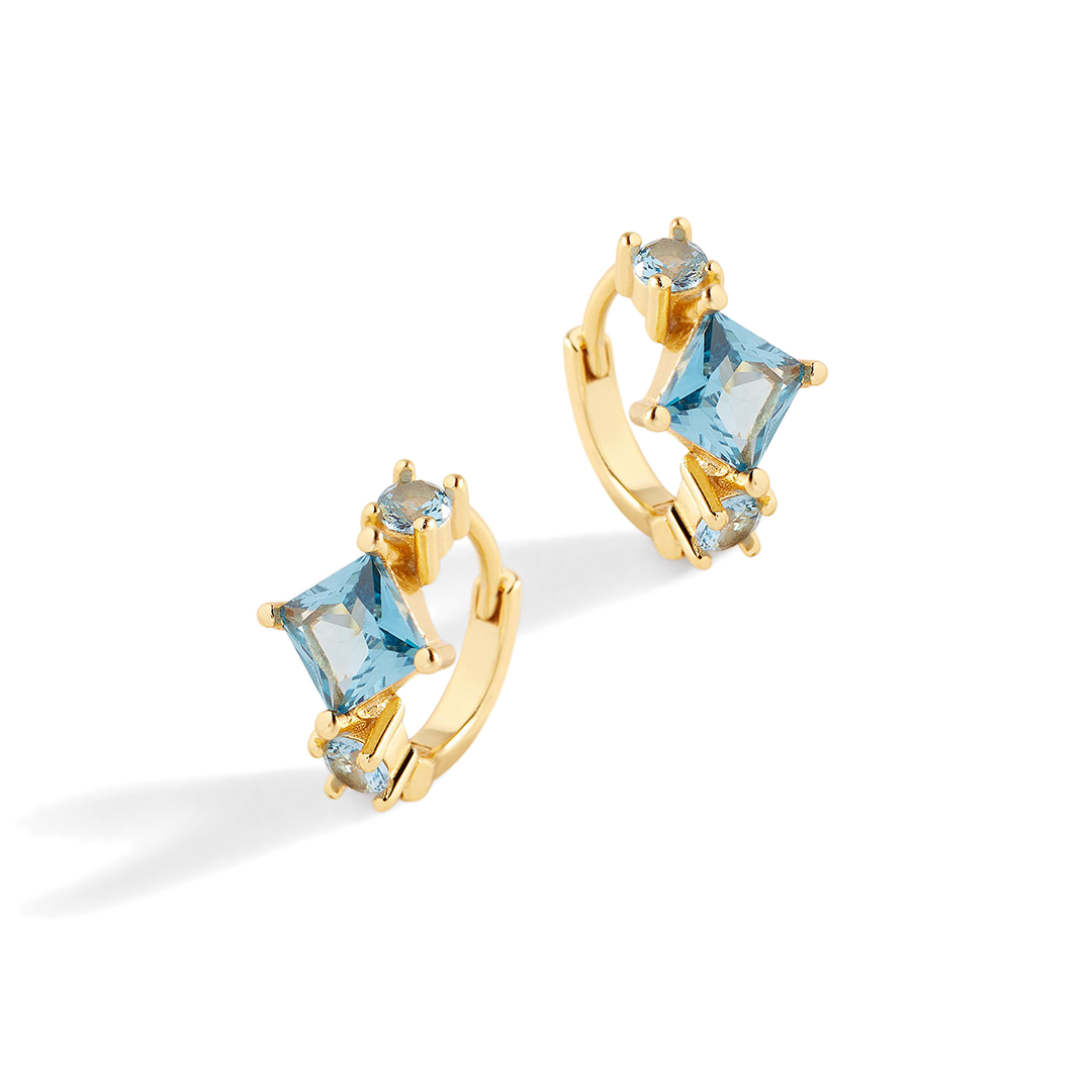 Gold hoop earrings with blue gemstones on a light gray background