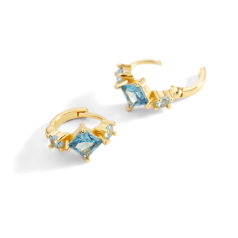 Gold hoop earrings with blue gemstones on a light gray background