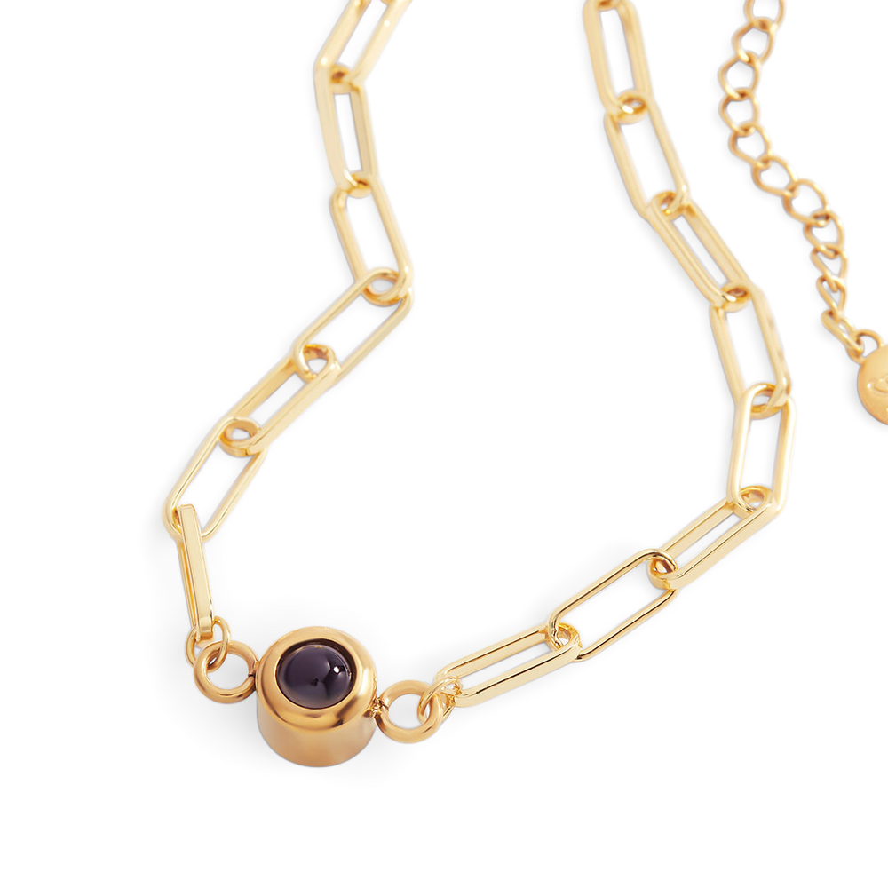 Gold chain necklace with a purple gemstone on a white background