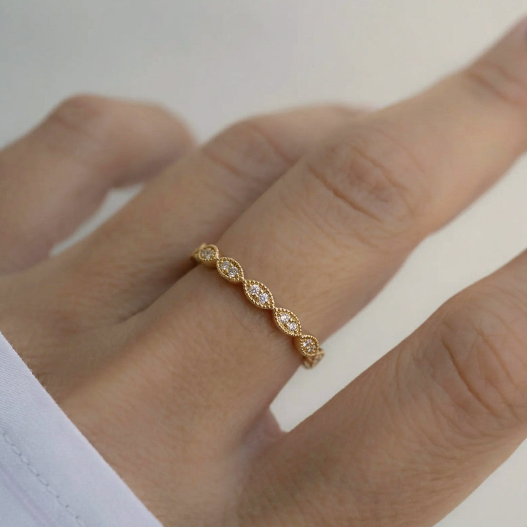 Gold ring with diamonds on a person's finger against a neutral background