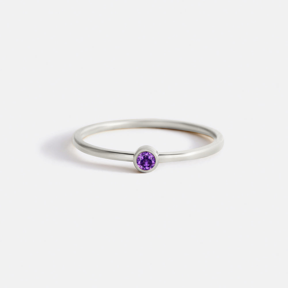 A gold-colored minimalist ring with a bezel-set purple birthstone.