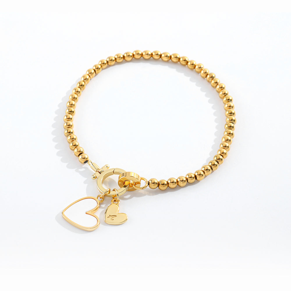 Gold beaded bracelet with heart and key charm on a white background