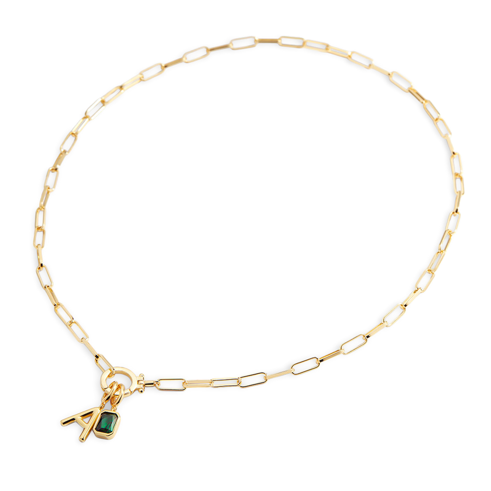 Gold bracelet with a green gemstone and letter charm on a light gray background
