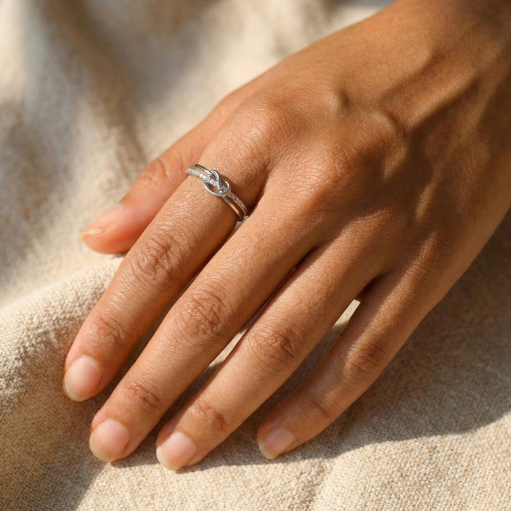 Hand wearing a silver ring on a beige fabric background