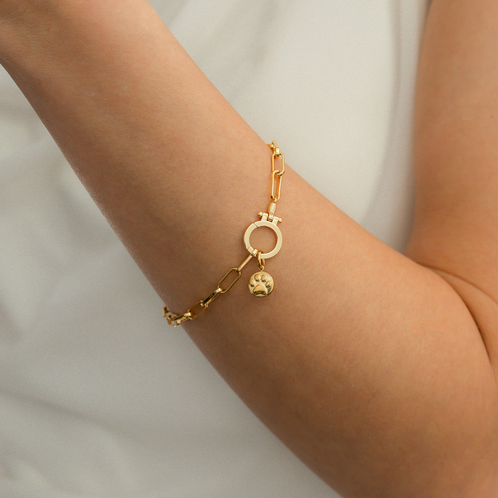 Gold bracelet with a small round charm on a person's wrist against a neutral background