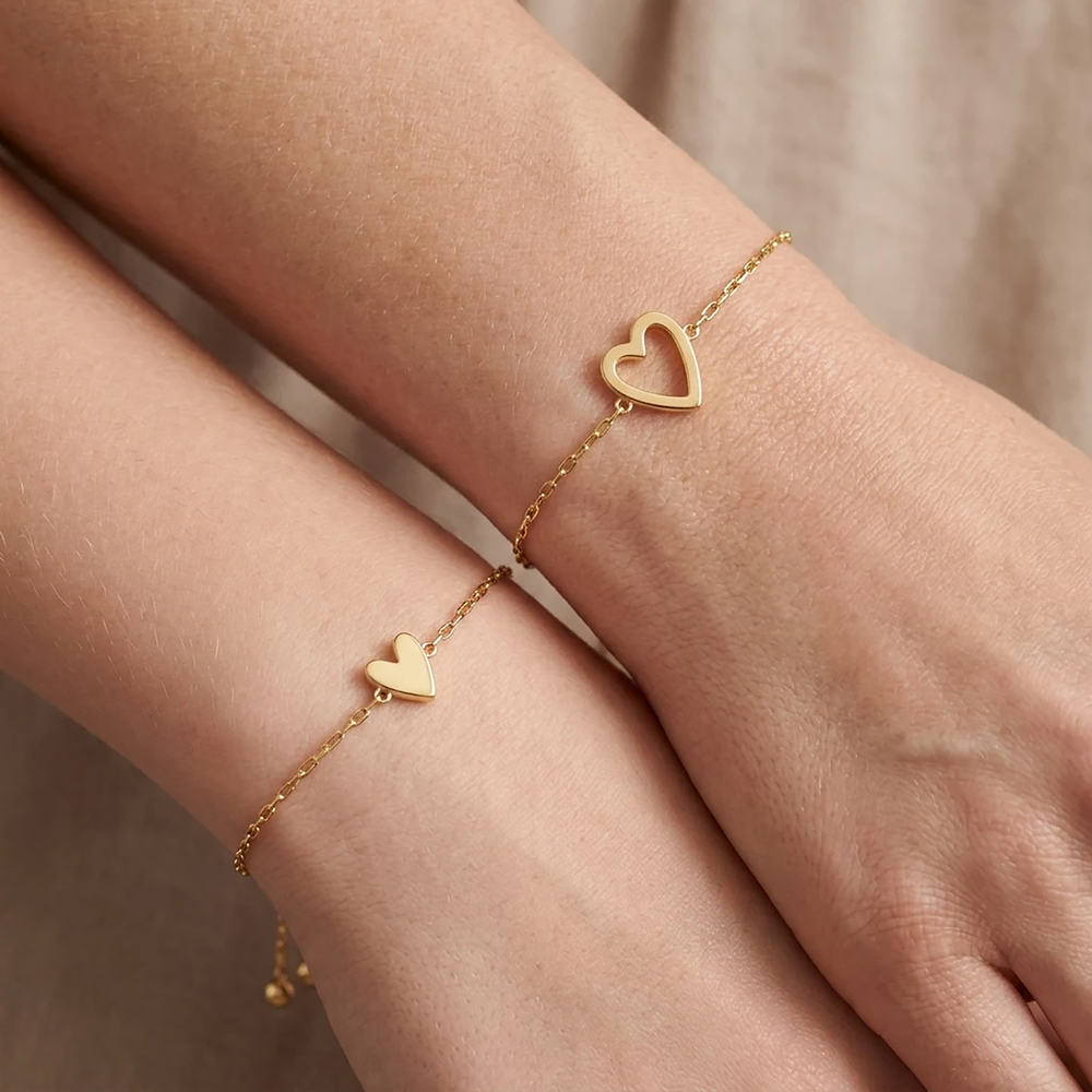 Gold heart-shaped bracelet on a wrist with a neutral background