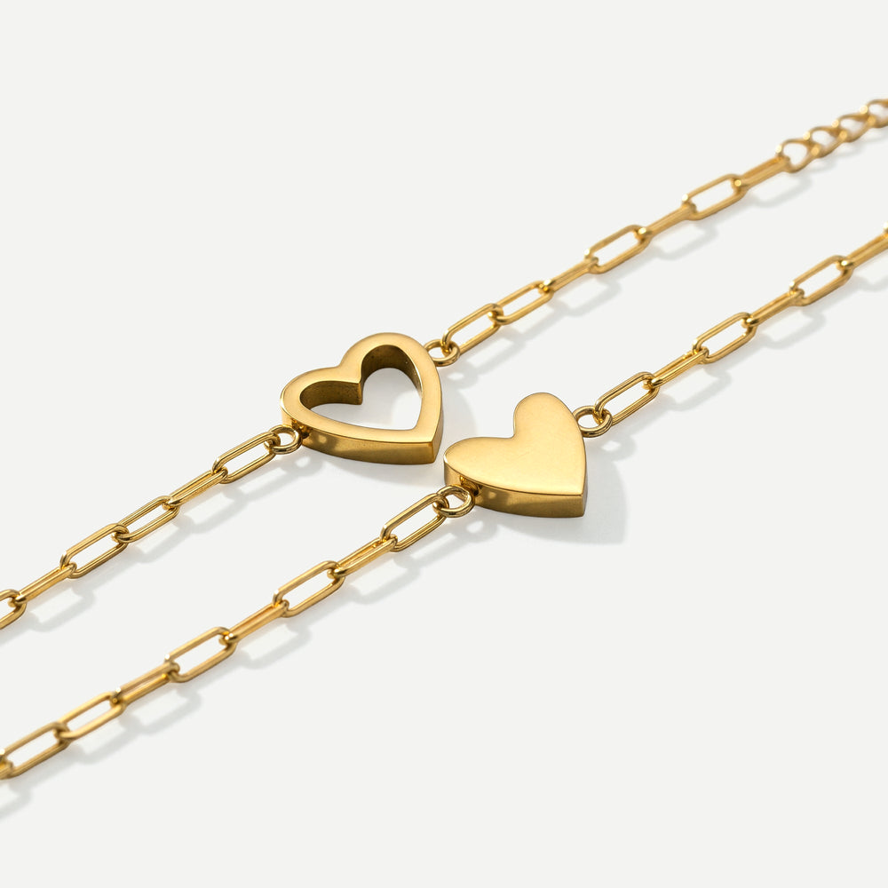 Two gold heart-shaped pendants on gold chains against a white background