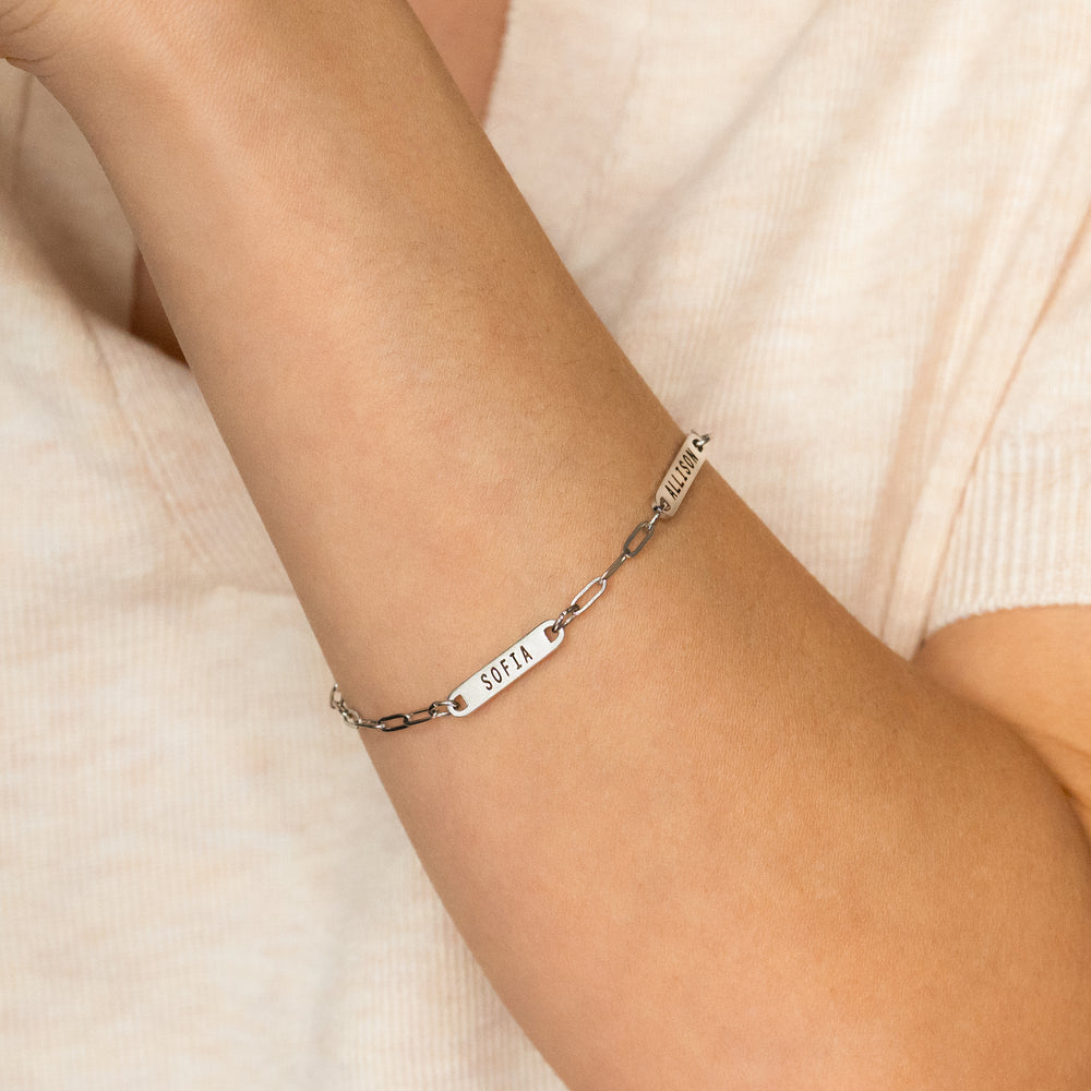 Silver bracelet with engraved name on a person's wrist against a soft beige background