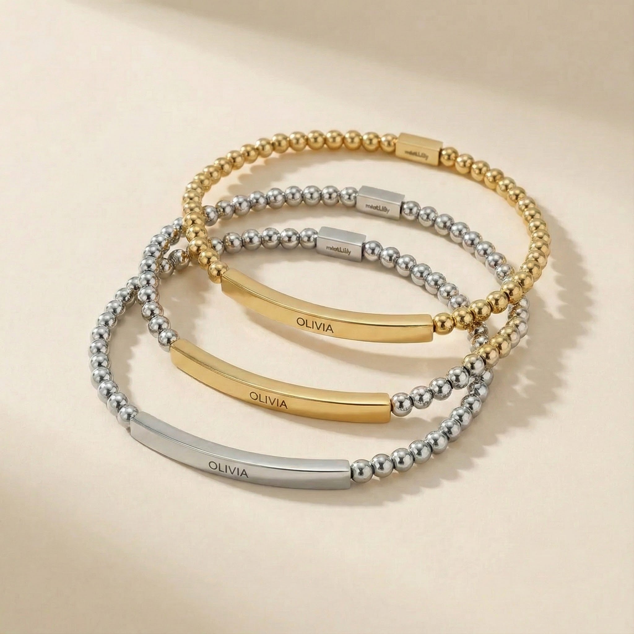 Three gold and silver bracelets with 'OLIVIA' engraving on a beige background