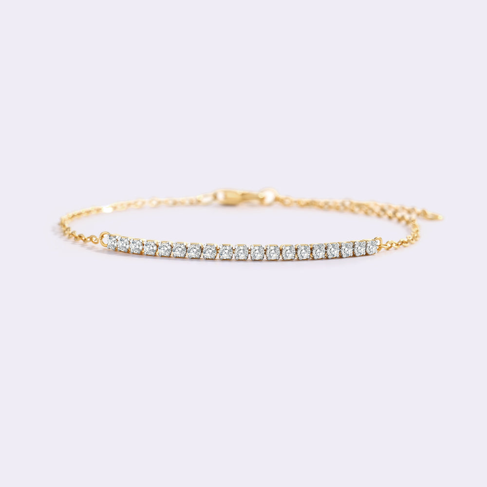 Gold petite line bracelet resting on a light surface, shown from a low angle with its row of stones in focus.