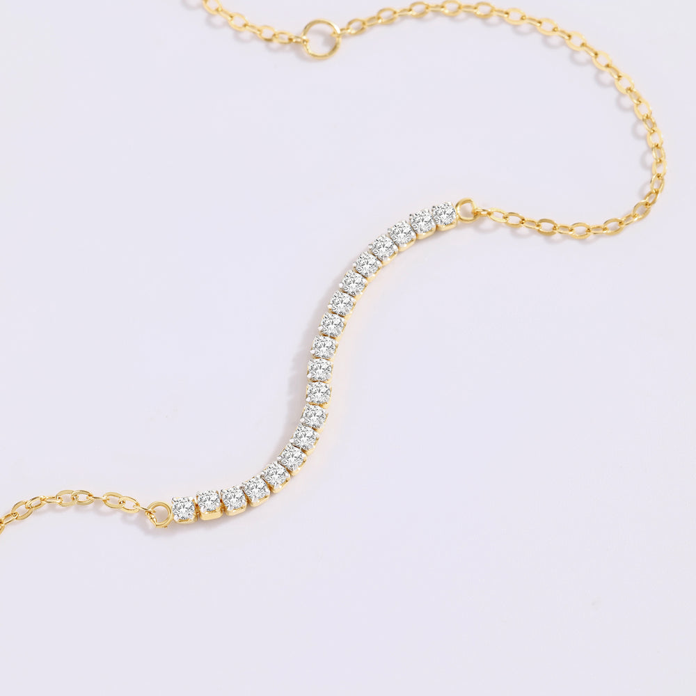 Close-up of the gold petite line bracelet's curved row of prong-set stones draped on a white background.