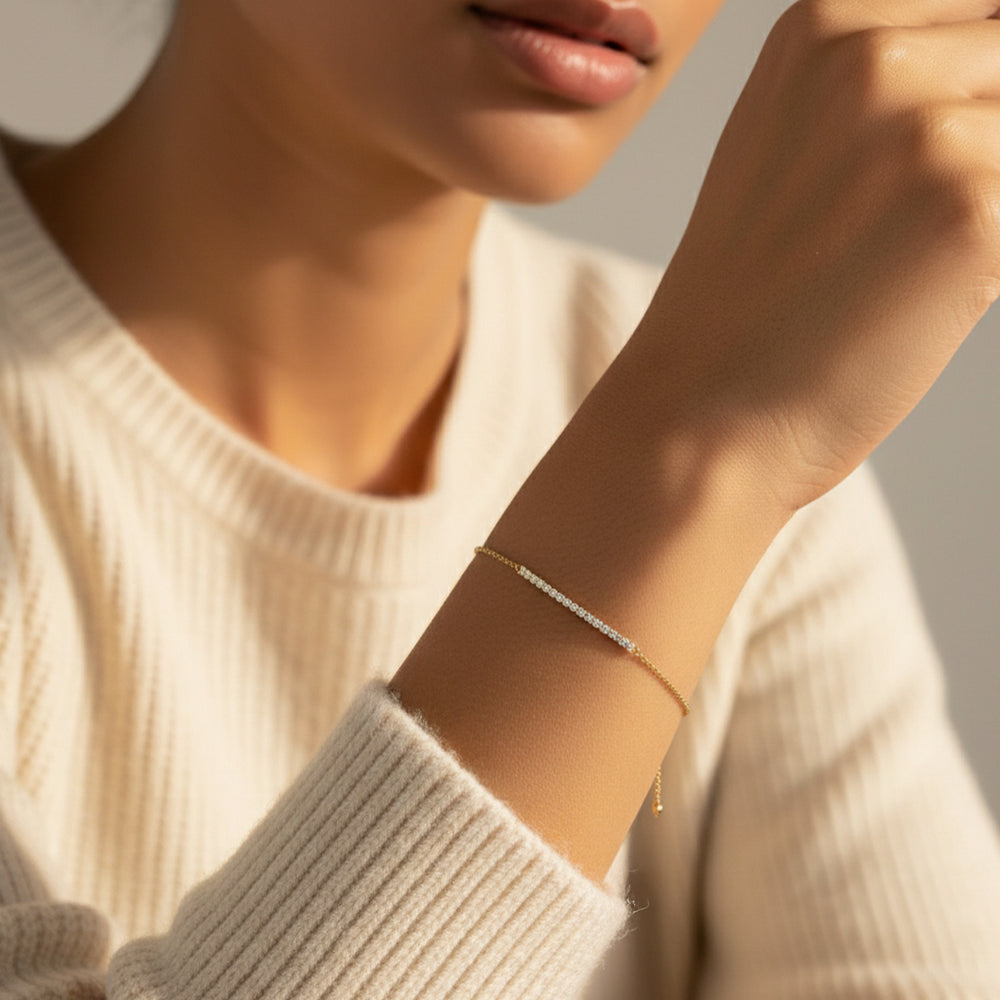 Model in a cream knit sweater wearing the gold petite line bracelet in warm natural light.