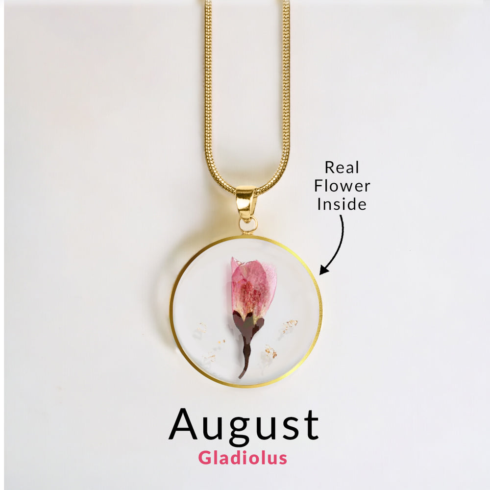 A gold-colored snake chain necklace with a round resin pendant containing a real red flower.