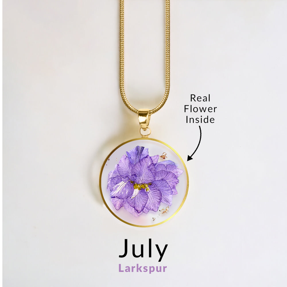 A gold-colored snake chain necklace with a round resin pendant containing a real red flower.