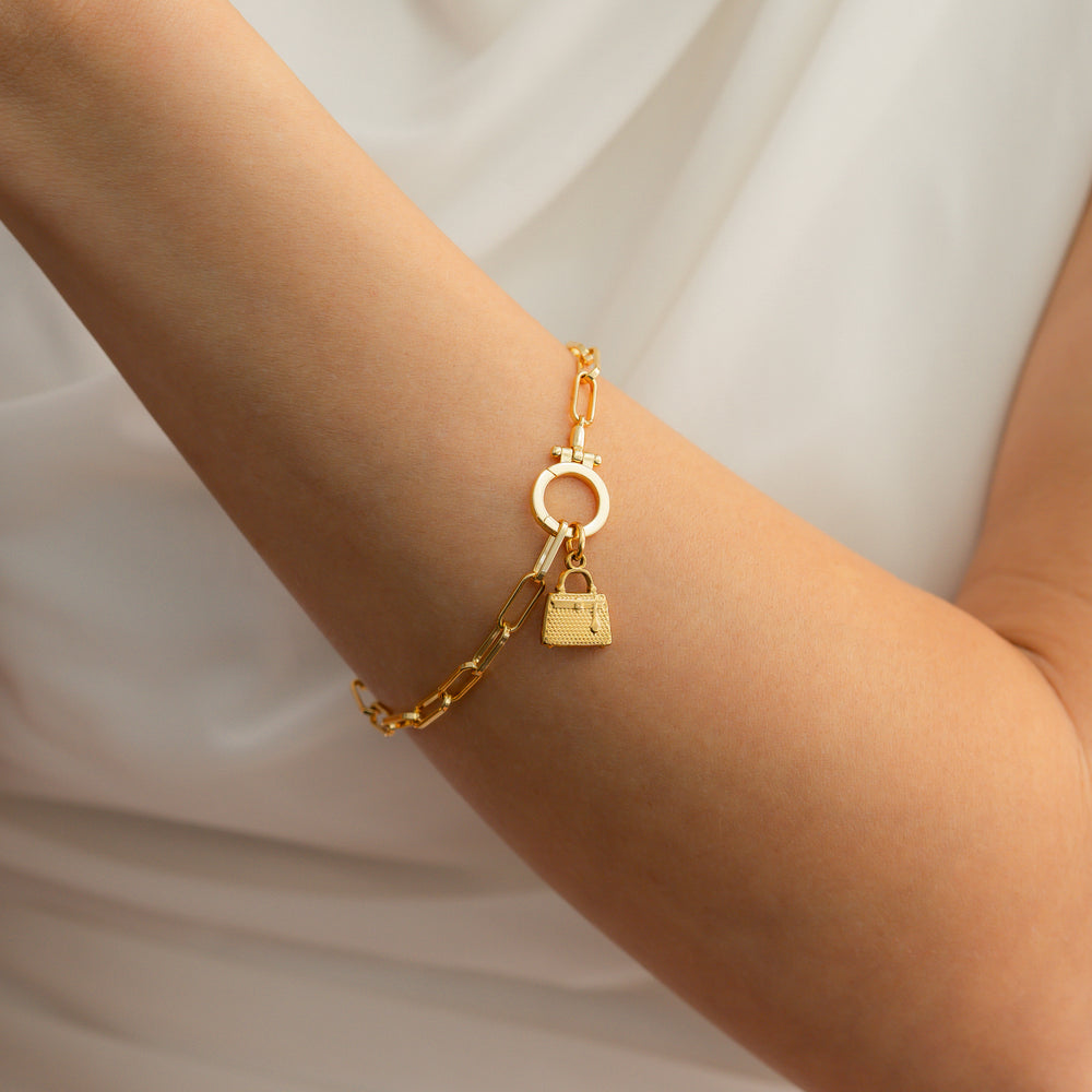 Gold chain bracelet with a lock charm on a wrist against a neutral background