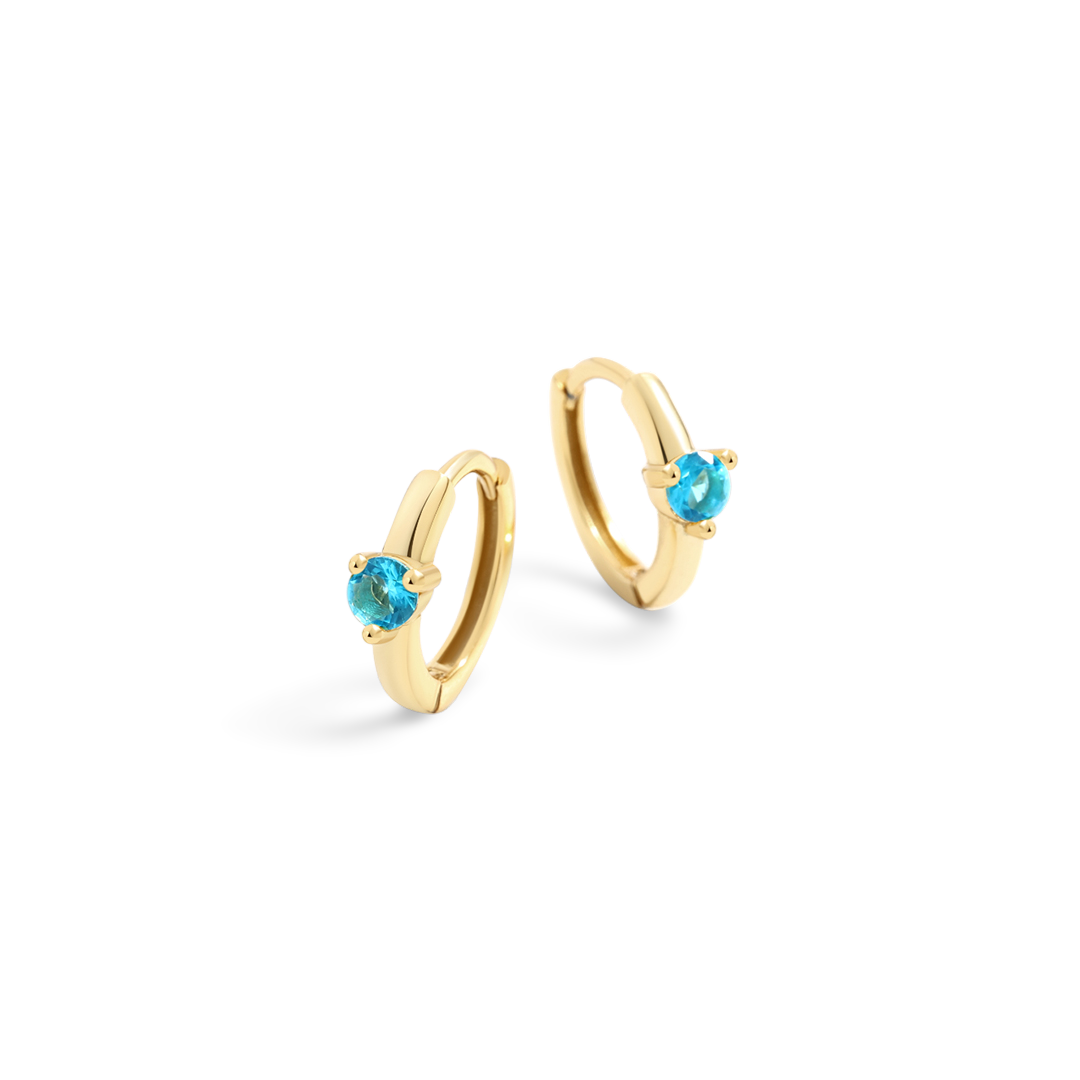 Gold hoop earrings with blue gemstones on a light gray background