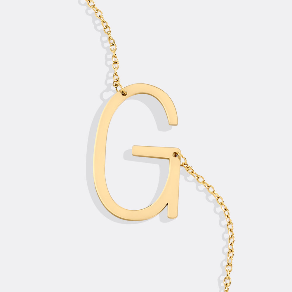Gold necklace with a letter 'G' pendant on a light gray background