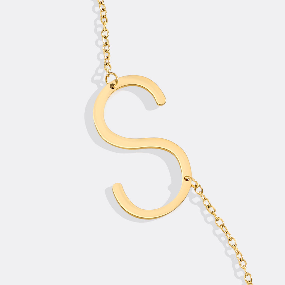 Gold necklace with a letter 'S' pendant on a light gray background
