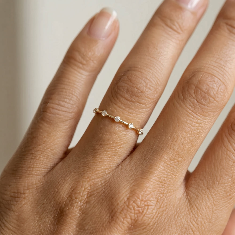 Close-up of a hand wearing a gold ring with small diamonds on a neutral background