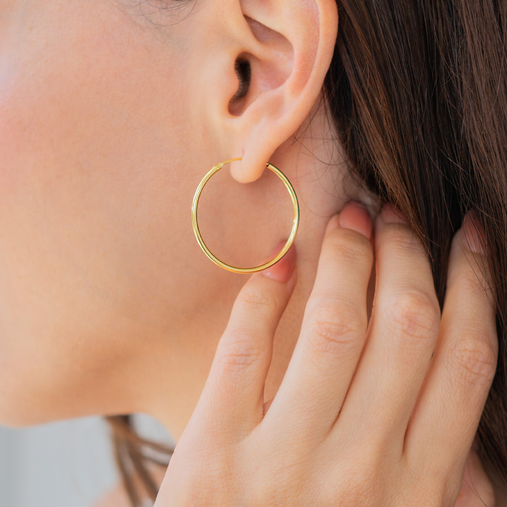 Gold hoop earring worn by a person with hand near ear