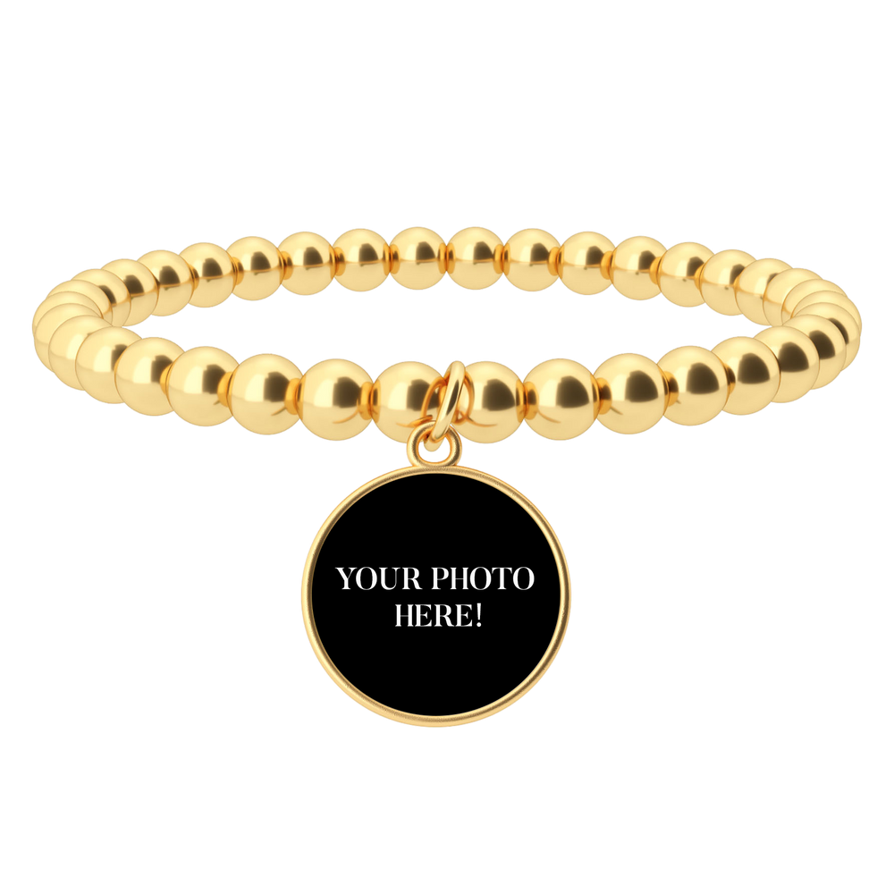 Gold beaded bracelet with a black round charm on a white background