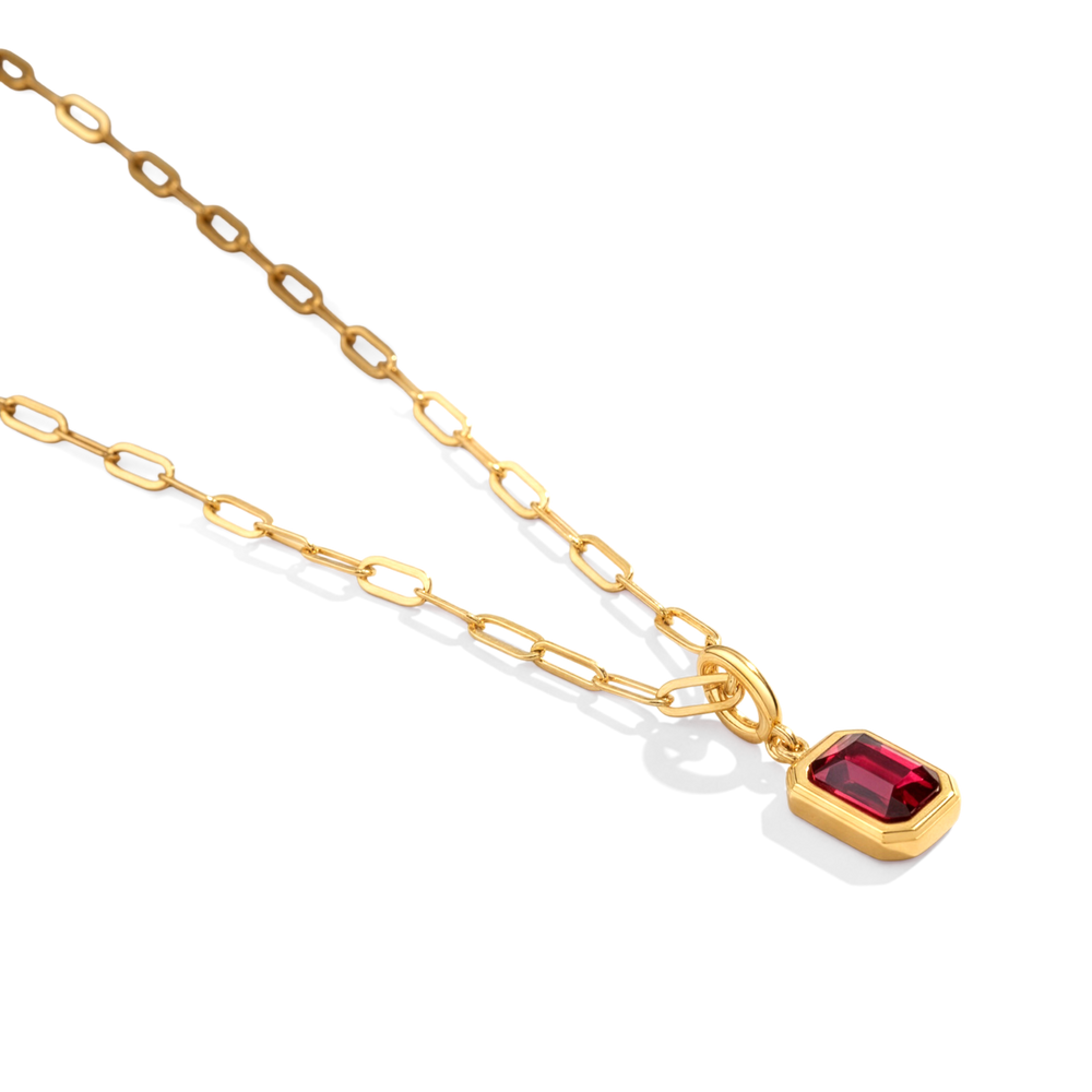 Gold necklace with a red gemstone pendant on a light gray background