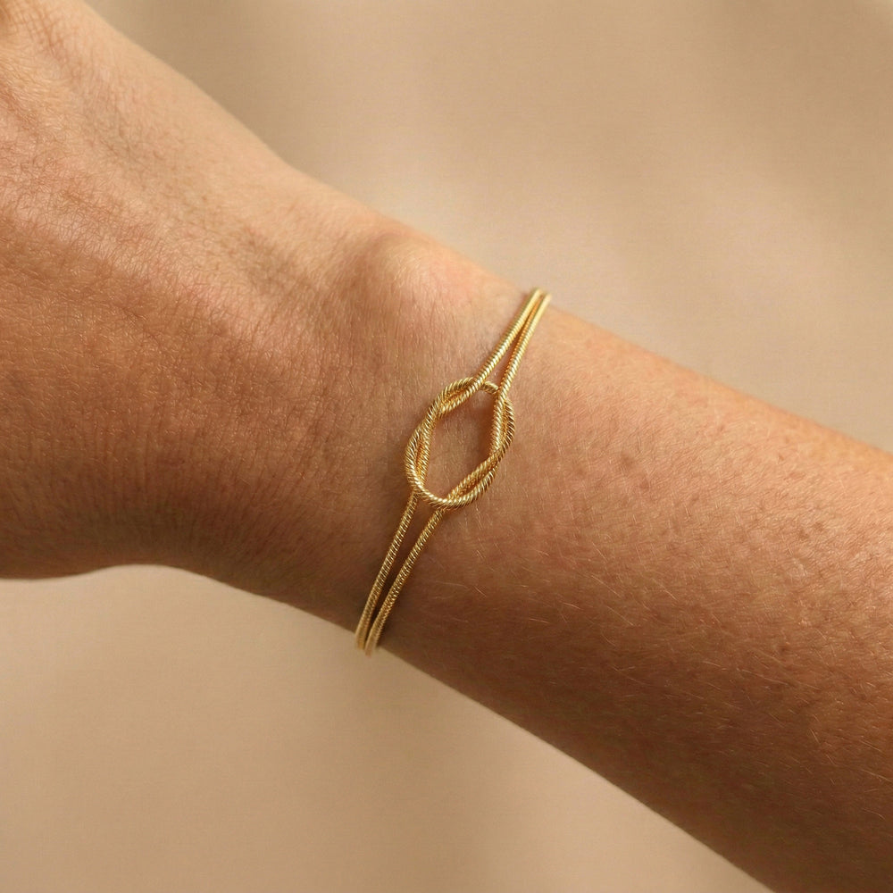 Gold bracelet on a wrist against a beige background
