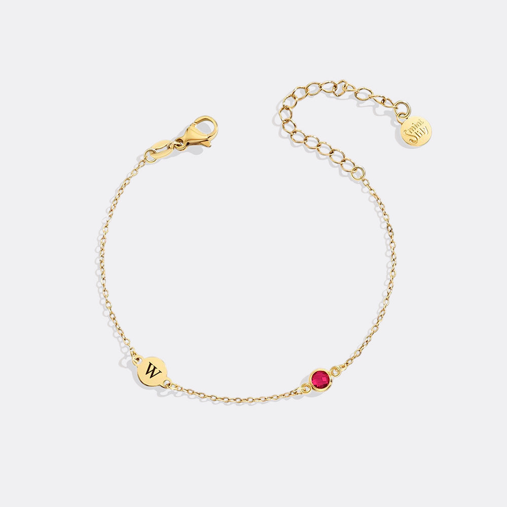 Gold bracelet with a red gemstone and letter 'W' charm on a white background